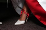 Bottom of bride's dress. white dress red trim, bride's foot, brides shoe, red ribbon.