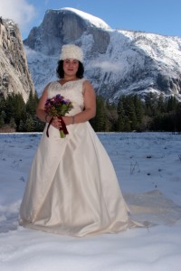Bride with fur cap in a snow covered meadow in front of snow capped half doom winter wedding in yosemite national park